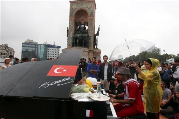 Una persona toca el piano mientras un manifestante lo cubre con un paraguas al pie del monumento a Mustafá Kemal Ataturk, fundador de la Turquía moderna, en la plaza Taksim de Estambul el viernes 14 de junio de 2013. (Foto AP/Thanassis Stavrakis)