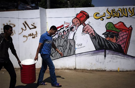 Partidarios del presidente egipcio depuesto Mohamed Morsi caminan junto a una pared pintada con grafito que dice en árabe "no al golpe" el jueves 25 de julio de 2013. El jueves el líder de la Hermandad Musulmana atacó con inusual dureza al jefe del ejército egipcio al decir que la deposición del presidente Mohamed Morsi era un crimen peor que destruir la Kaaba, el lugar más sagrado del islam. (Foto AP/Khalil Hamra)