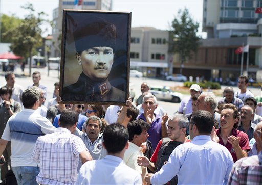 Un hombre sostiene un cartel con una imagen de Mustafa Kemal Ataturk a la espera de entrar al parque Gezi en la plaza Taksim en Estambul, Turquía, el lunes 8 de julio de 2013. El gobierno había anunciado que abriría el parque pero lo cerró poco después cuando los manifestantes empezaron a dirigirse hacia la zona para realizar un mítin. (Foto AP/Gero Breloer)