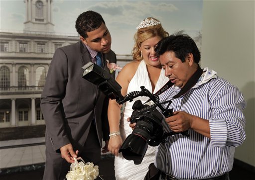 Braulio Cuenca le muestra a Jorge Mejía e Irma Aguilar las fotos que tomó de su boda en el registro civil de Nueva York el 7 de agosto del 2013. Cuenca es un ecuatoriano que lleva 20 años fotografiando bodas en Nueva York y a menudo sale de testigo. (AP Photo/Richard Drew)