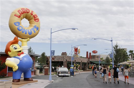 Visitantes pasan frente a la tienda de rosquillas Lard Lad Donuts, izquierda, y los Jardines Duff en la zona temática Springfield USA en los Estudios Universal en Florida, el jueves 5 de septiembre de  2013, en Orlando, Florida. Creada alrededor del juego mecánico de Los Simpson que se inauguró en 2008 la nueva zona del parque tiene comida sabrosa pero insalubre que aparece en el programa. (Foto AP/John Raoux)