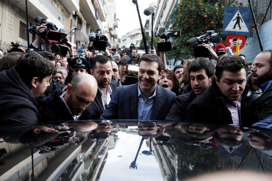 El líder del partido de la izquierda radical Syriza,Alexis Tsipras (centro), envuelto en una nube de medios de comunicación intenta llegar a su coche tras votar en Atenas, el 25 de enero de 2015. (Foto AP/Petros Giannakouris)