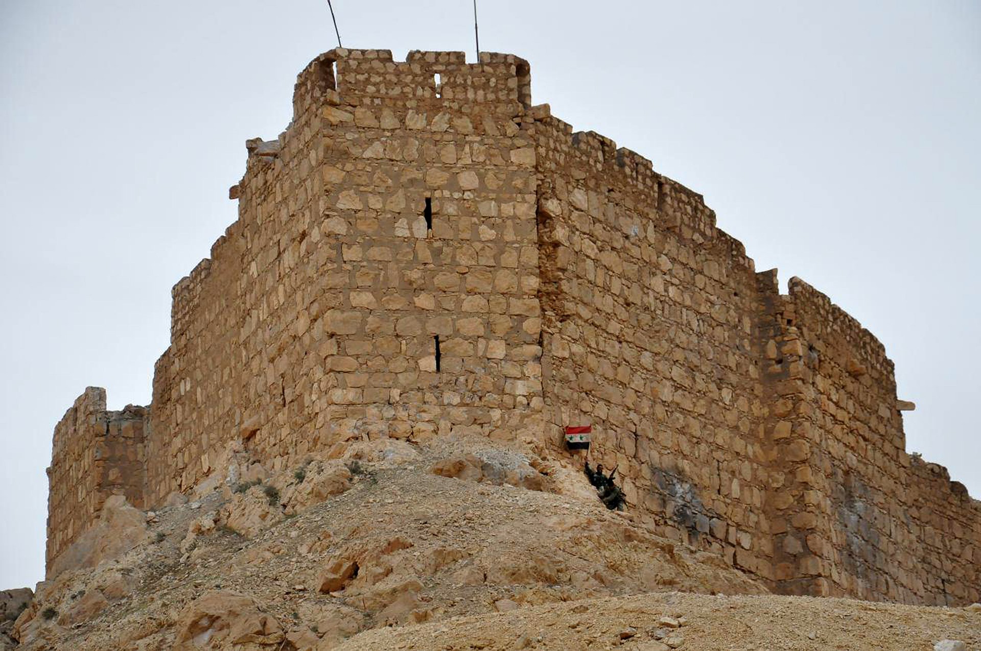 Un soldado sirio celebra con su bandera a los pies de uno de los edificios que sobrevivió a la batalla - Crédito: AP