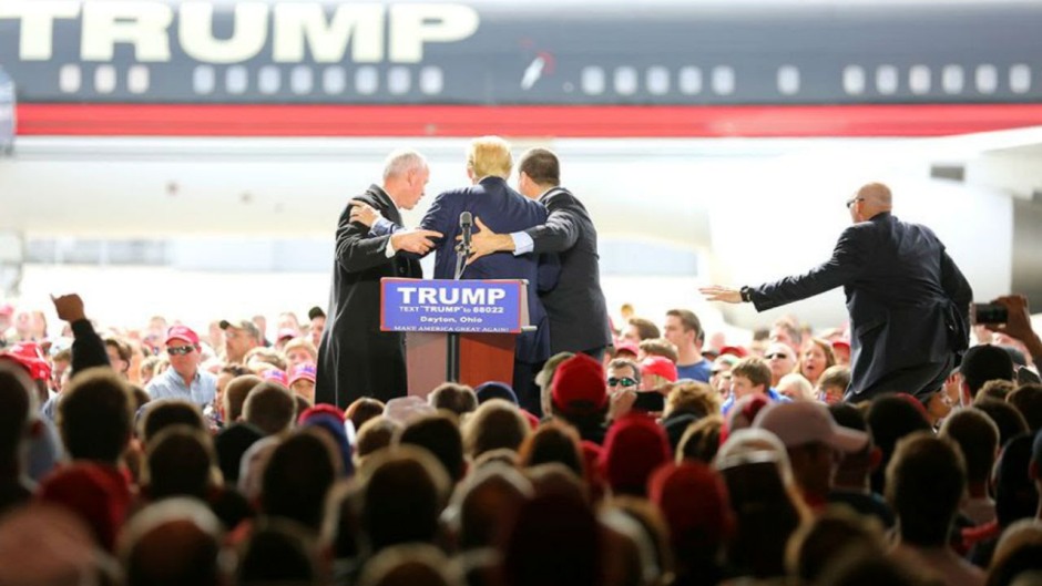 Personal de seguridad rodea al precandidato presidencial republicano Donald Trump después de que un hombre intentó subirse al escenario durante un mitin de campaña en Vandalia, Ohio, en las afueras de Dayton, el sábado 12 de marzo de 2016. El hombre fue detenido y Trump continuó con su discurso. (Carrie Cochran/The Cincinnati Enquirer vía AP)