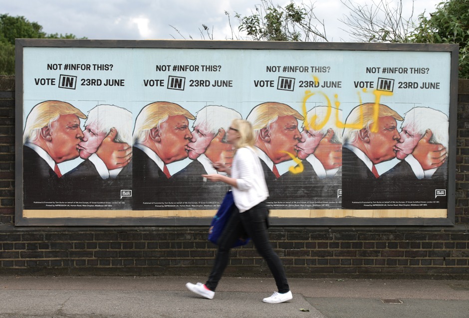 Una mujer camina frente a carteles a favor de votar por la permanencia de Gran Bretaña en la Unión Europea, en Londres, 21 de juniio de 2016. En el cartel aparece el candidato republicano estadounidense Donald Trump besando al principal partidario de la salida británica, Boris Johnson. (Yui Mok / PA via AP)