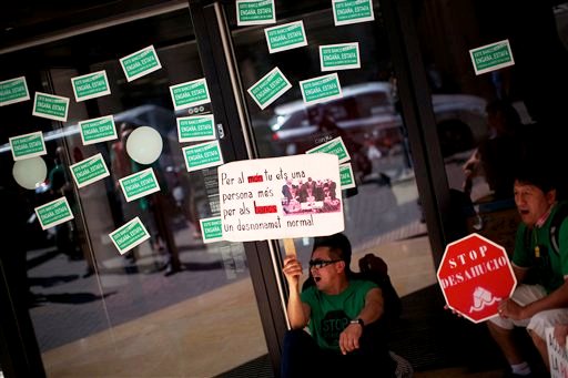 Manifestantes se sientan en la entrada principal de un banco durante una protesta contra las previsibles ejecuciones y desahucios de propiedades por los retrasos en el pago de hipotecas en Barcelona, España, el jueves 31 de mayo del 2012. La Unión Europea urgió el jueves que España presenté un plan claro de cómo planea financiar al sector bancario, advirtiendo que la incertidumbre en el sector ha contribuido a la reciente agitación de los mercados y el incremento de los costos de la emisión de deuda. La pancarta que sostiene el manifestante dice en catalán "Para el mundo tu eres otra persona, para el banco eres solo una ejecución" (AP Foto/Emilio Morenatti)