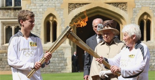 En esta imagen suministrada por el comité organizador de los Juegos Olímpicos, la reina Isabel II, segunda desde la derecha, y el Duque de Edimburgo observan a los portadores de la antorcha olímpica, Gina Macgregor, derecha, y Phillip Wells, a las afueras del castillo Windsor el martes, 10 de julio de 2012, en Inglaterra. (AP Photo/Chris Radburn/LOCOG)