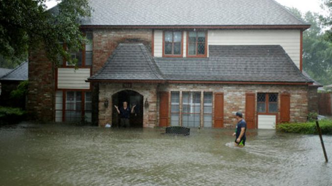 Un hombre parado en la entrada de su inundada casa responde a una oferta para ayudar a sacarlo en un vecindario que quedó inundado con el agua de las lluvias que dejó el huracán Harvey a su paso el lunes 28 de agosto de 2017 en Houston, Texas. (AP Foto/Charlie Riedel)