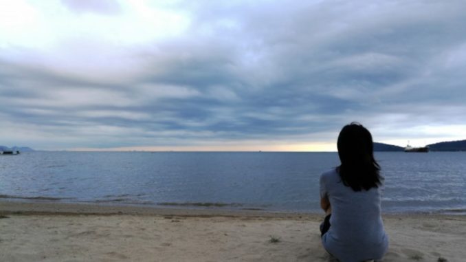 mujer-sentada-sola-playa-cielo-nublado-atras_28991-107