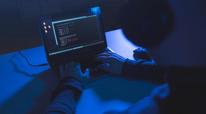 hacker with coding on laptop computer in dark room