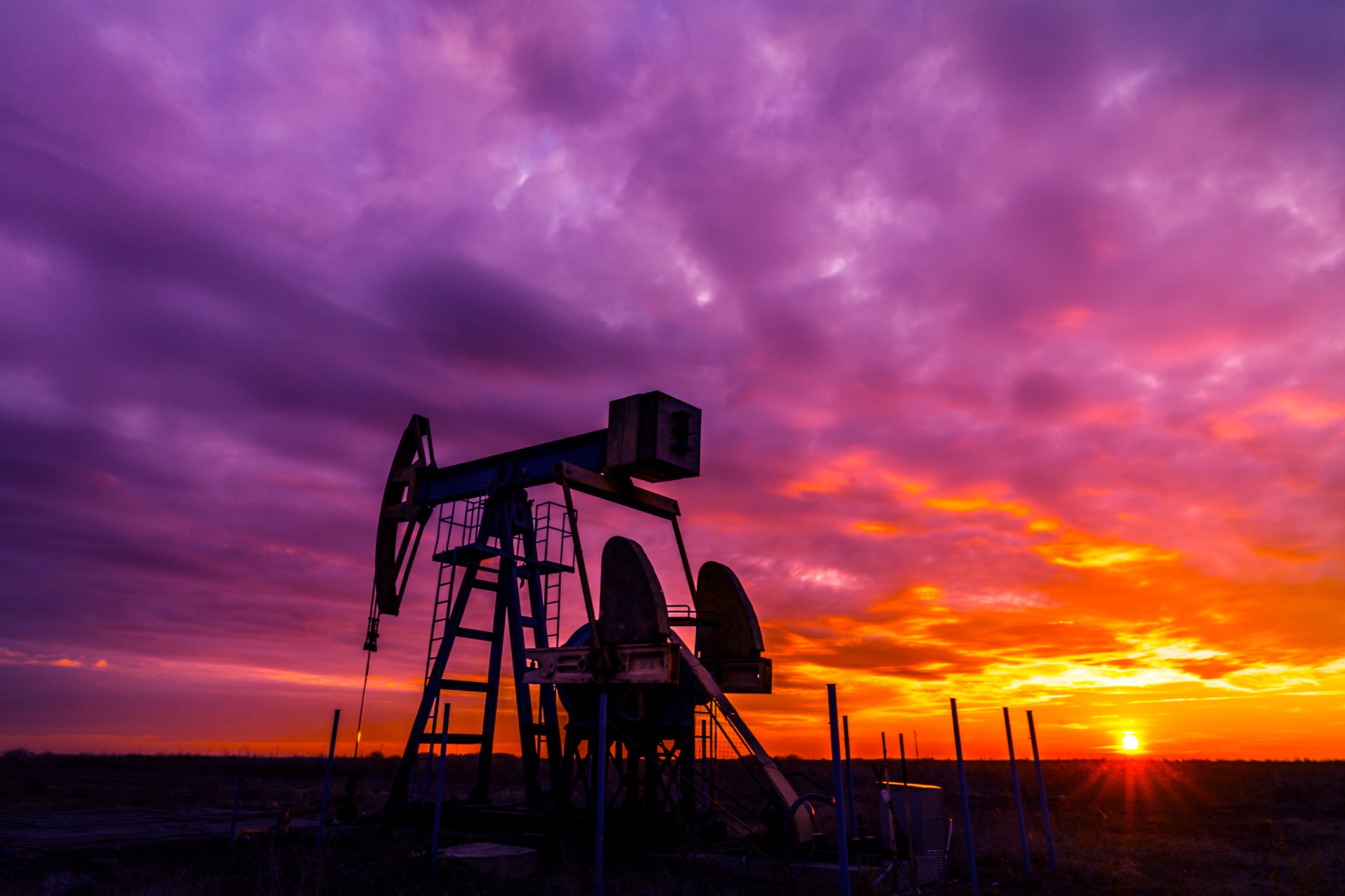 Scenery with oil and gas well pump and dramatic sunset
