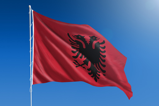 The National flag of Albania blowing in the wind in front of a clear blue sky