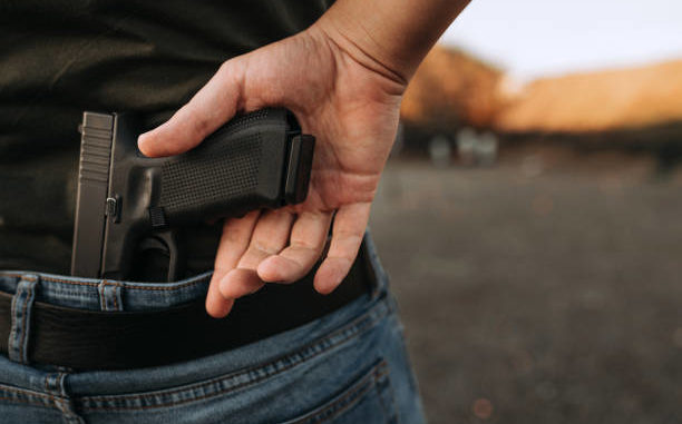 Man conceals a gun in the back of his pants, outdoors.